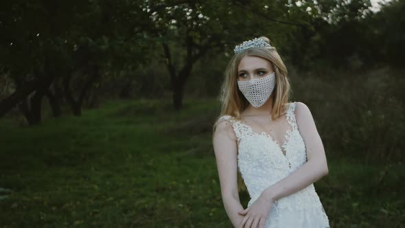 portrait of the bride in a mask posing. Beautiful young bride in a wedding dress in the park. She ha