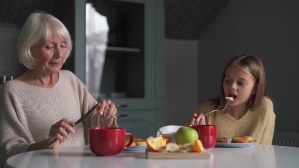 Laughing grandmother and granddaughter eating breakfast