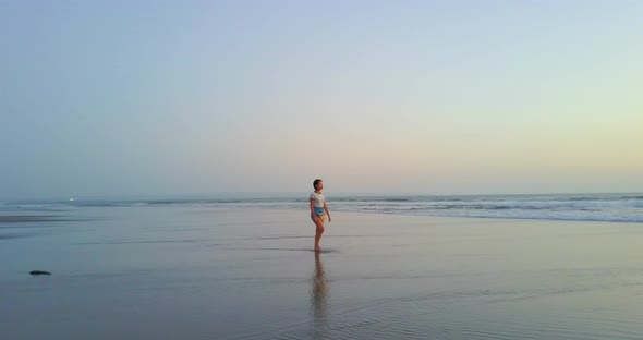 Aerial drone view of a young woman walking on the beach at sunset.