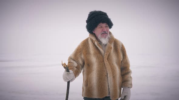 Zoom Out Free Old Indigenous Man Walking in Slow Motion Looking Around White Snowy Northern Desert