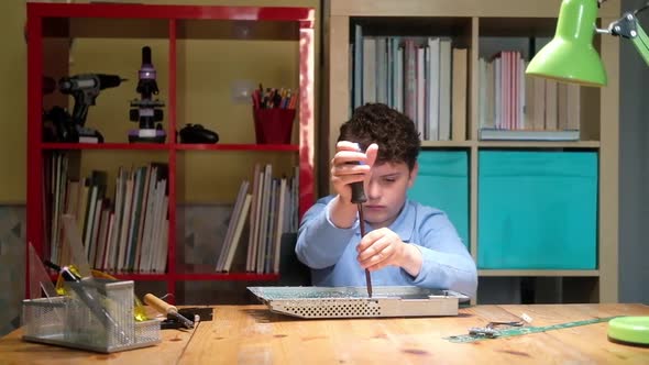 Schoolboy boy unscrews chip with screwdriver to work with soldering iron.