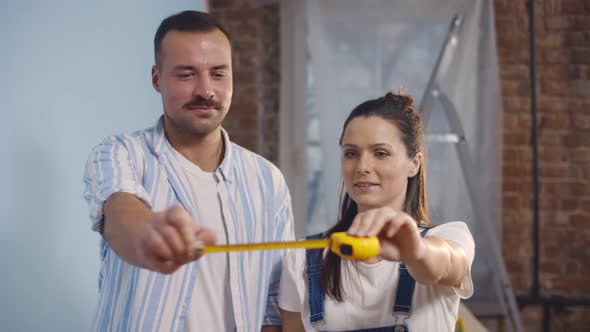 Lovely Young Couple with Tape Measure Discussing Renovation Process