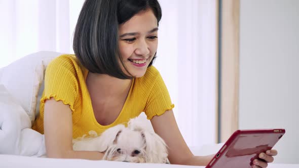 Young woman using tablet in bed with her Maltese dog.