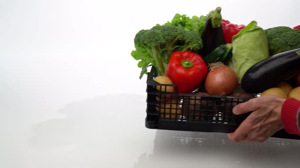 A Volunteer Distributor Handing a Box to a Masked Woman with Fresh Vegetables for Those in Need