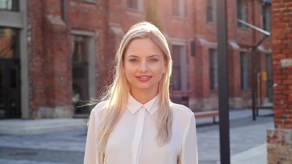 Cute Beautiful Dreamful Blonde Girl in a Light White Shirt Walking Along City