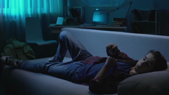 Male Teenager Lying on Sofa and Watching TV Show at Night, Weekend Leisure