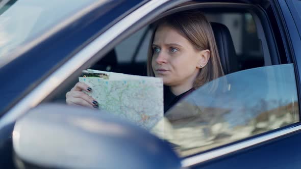 Lost Troubled Caucasian Young Woman Sitting on Driver's Seat in Car Examining Paper Map