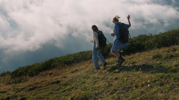 Two Young Women are Walking Together in Highlands Above Clouds at Summer Vacation