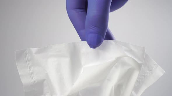 A hand in blue protective medical gloves takes, pulls a white paper facial tissue 