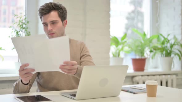 Man with Laptop Reading Documents in Office