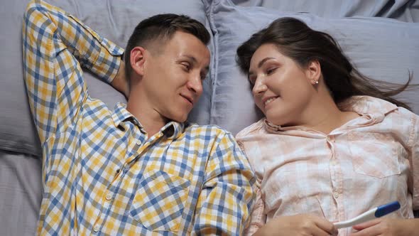 Man and Woman Talking While Lying in Bed Discussing Pregnancy Test Top View