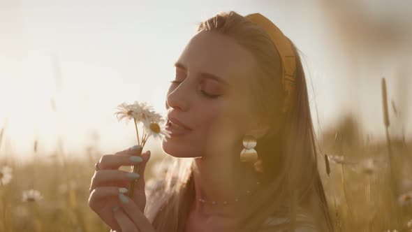 A Happy Woman is Sniffing of Chamomile on Field at Sunset