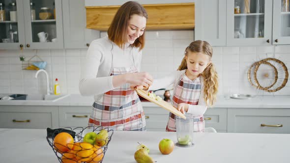 Cute Girl Pouring Out Cut Apples Cooking Smoothie with Mother at Kitchen Slow Motion