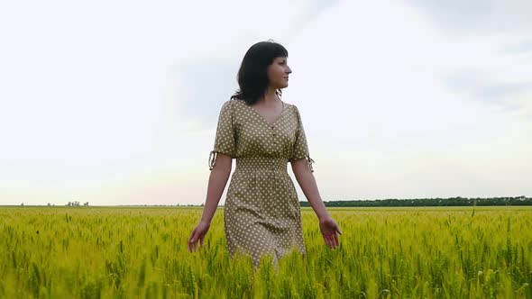 A Young Girl Walking Happily in Slow Motion Through a Green Field, Touching the Ears of Wheat