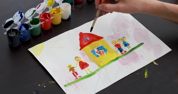 Child Draws House and Family Picture with Brush in Gouache