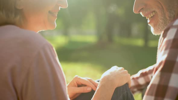 Smiling Retired Couple Relaxing in Park, Holding Hands and Talking About Love