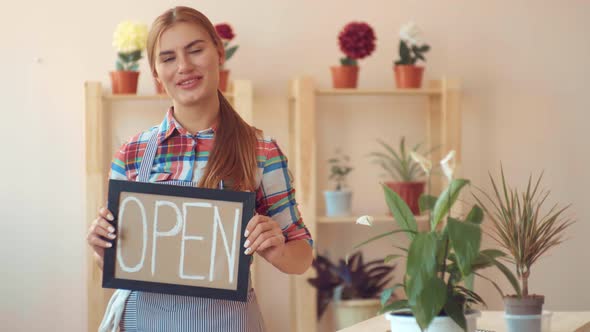 Small Business. Opening a Flower Shop. Girl in a Plaid Shirt and Striped Apron with an Open Sign