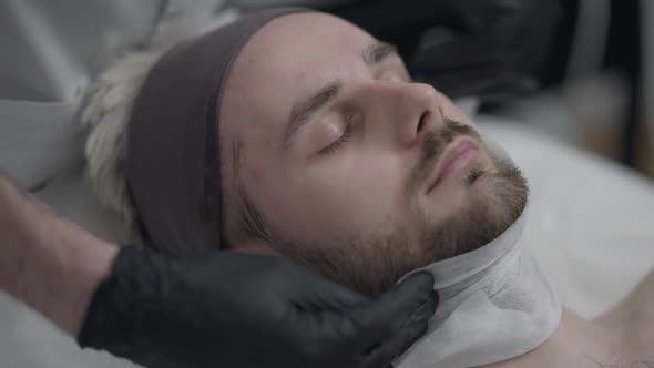 Closeup of Young Handsome Caucasian Man with Hands of Beautician Drying Up Skin with Wipe