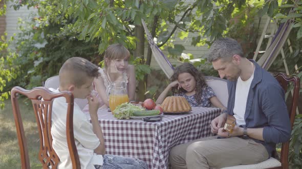 Father Plays the Guitar for His Family at a Dinner Table Sitting in the Backyard. Friendly Family