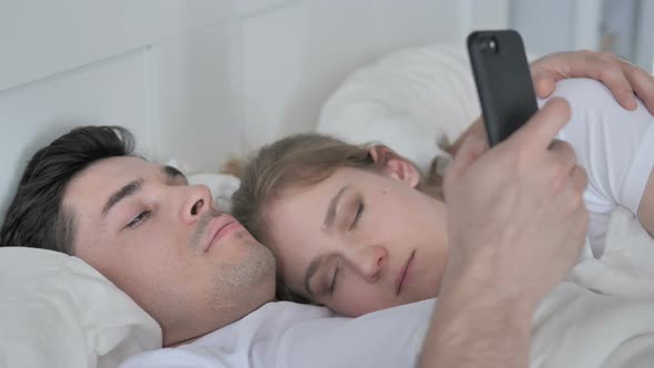 Man Using Smartphone While Cuddling Sleeping Girlfriend