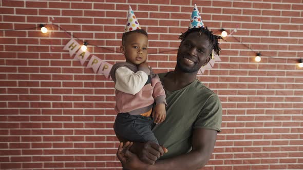 Portrait of Cute Afroamerican Boy on Fathers Arms in Bday Hats