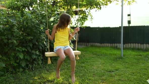 Happy barefoot laughing child girl swinging on a swing