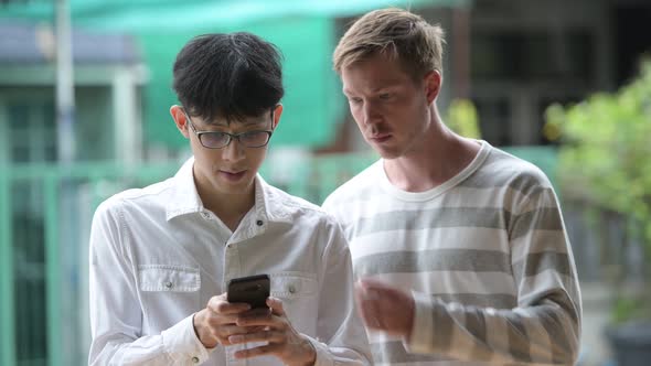 Two Multi-ethnic Businessmen Using Phone Together in the Streets Outdoors