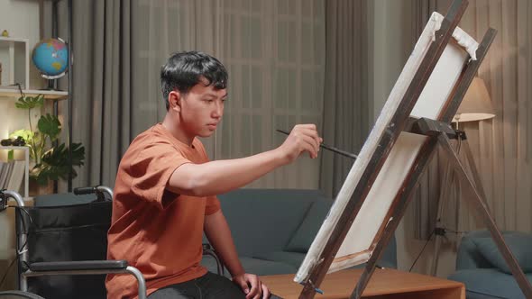 Asian Artist Boy In Wheelchair Holding Paintbrush Mixed Colour And Painting On The Canvas