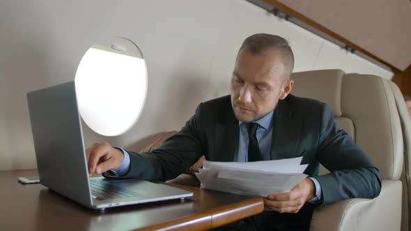 Attractive Businessman Working with Documents and Laptop in Aircraft