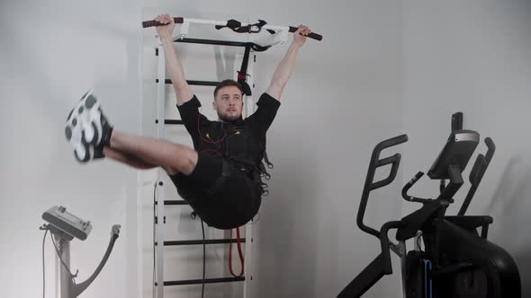 Concentrated Man Wearing Electrostimulation Equipment  Hanging By the Stand and Pulling His Legs Up