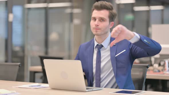 Businessman Showing Thumbs Down Sign While Using Laptop in Office