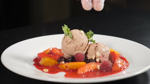 Pignolia Nuts Falling on Fruit Dessert with Ice-cream. Slow Motion. Confectioner Pouring Pinenuts on