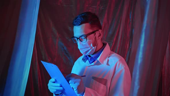 Portrait of male doctor fills out medical form on clipboard.