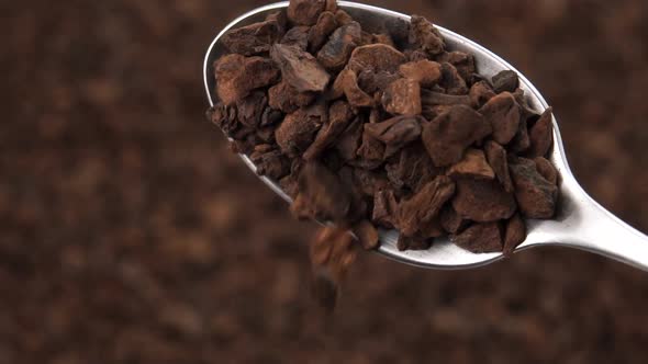 Particles of dried roasted chicory root fall from a teaspoon in slow motion into a heap in blur