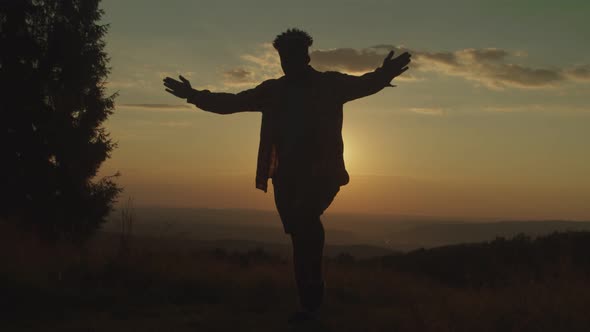 Silhouette of Active Man Standing in Balancing Karate Kid Yoga Pose on Mountain Top at Sunset