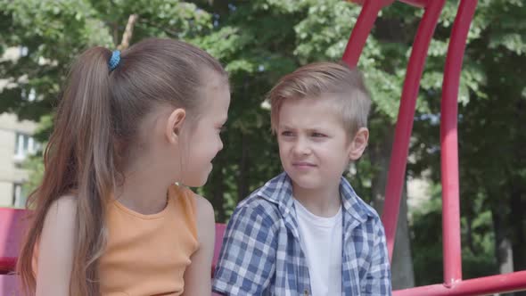 Cute Boy and Girl Sitting on the Swing Close Up in the Park, Looking at Each Other with Tenderness