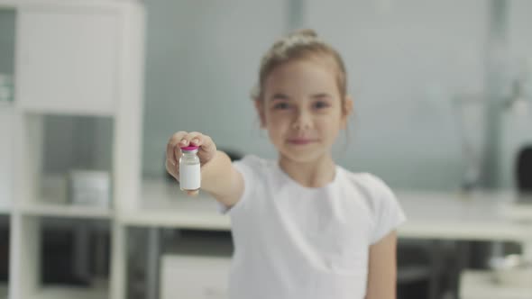 A Cute Girl in a White Tshirt Shows a Bottle of Vaccine to the Camera and Smiles Variable Focus