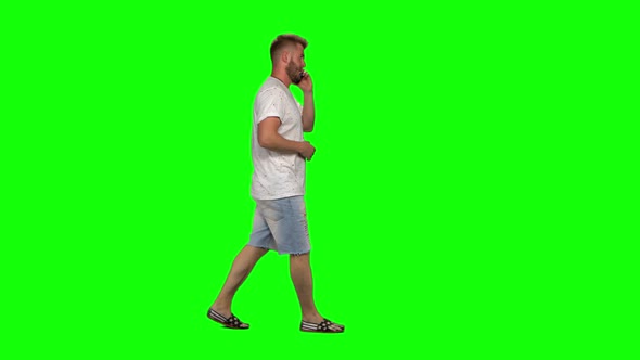 Bearded Guy Calmly Walking and Talking on the Mobile Phone on Green Screen Background. Chroma Key