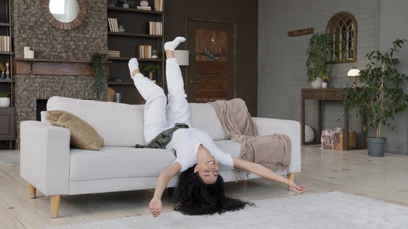 Young Crazy Funny Carefree Woman Lying Upside Down on Cozy Sofa in Living Room Shaking Arms and Legs