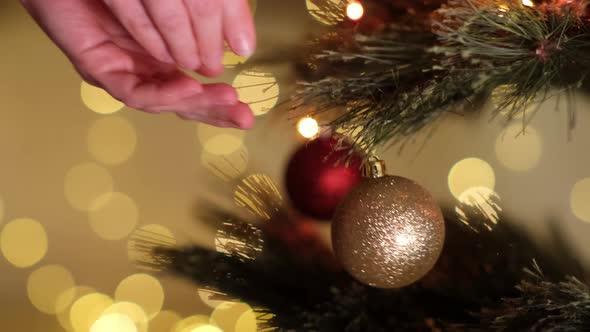 Woman Hand Hanging Decorative Gold Ball on Christmas New Year Tree Branch Against Background of alt