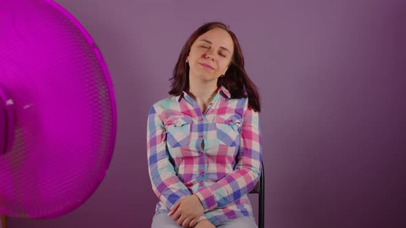 Close Up of Young Woman Sitting on Chair in Front of Fan on Purple Background