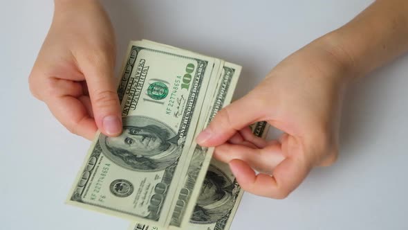 A Woman Counts Dollar Bills for 100 Dollars on a White Background Top View