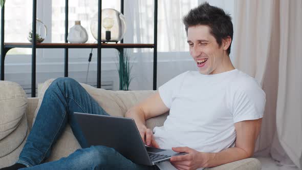 Caucasian Millennial Cheerful Business Man Adult Lies Sitting on Couch at Home Looking at Laptop