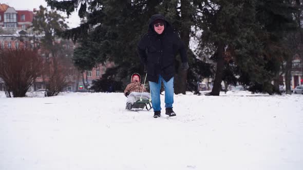 Father pulling cheerful kid on sled