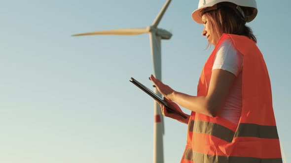 Female an Engineer in a Helmet and an Orange Vest Controls the Operation of a Wind Turbine Using a