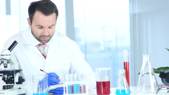 Scientist Writing Details While Working on Microscope in Laboratory