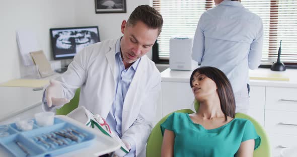 Caucasian male dentist with dental nurse examining teeth of female patient at modern dental clinic