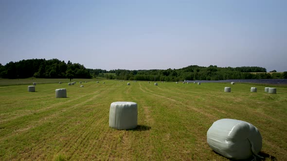 Plastic-Wrapped Hay Bales on a farm field after harvesting - aerial backward dolly