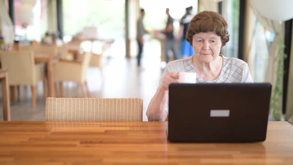 Senior Woman Drinking Coffee While Using Laptop At The Coffee Shop