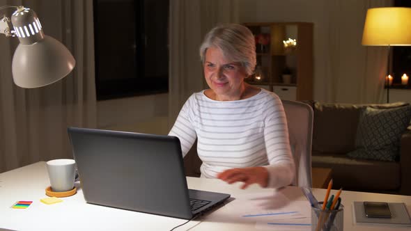 Happy Senior Woman with Laptop at Home in Evening